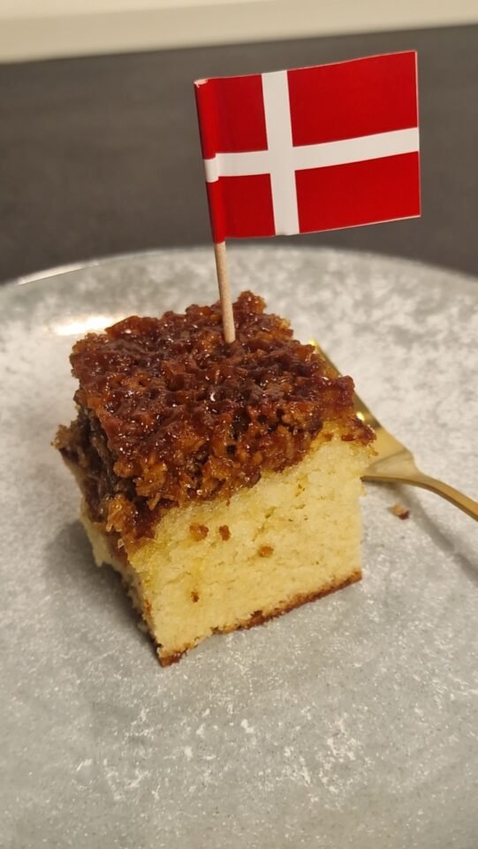 Slice of Drømmekage fra Brovst topped with a small Danish flag