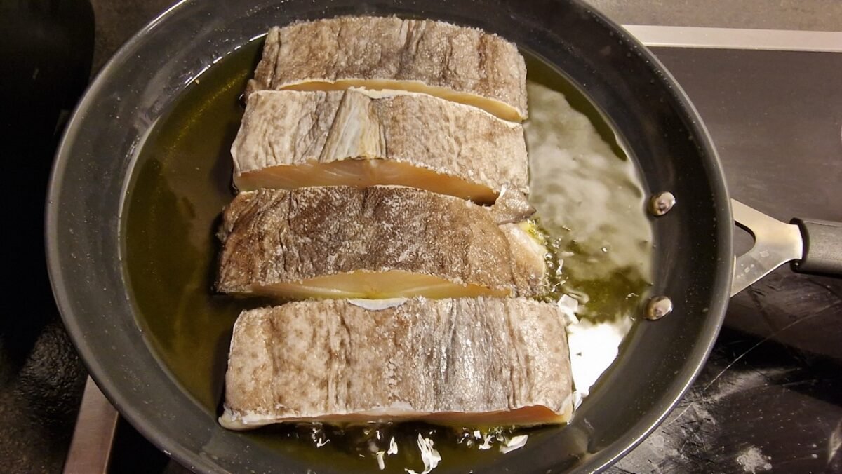 Cod cooking in olive oil, skin-side up