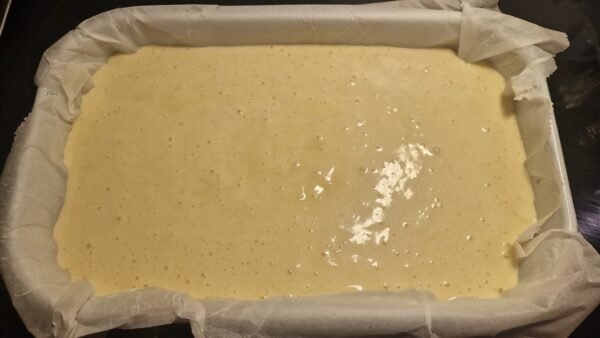 Cake batter in a rectangular pan lined with parchment paper