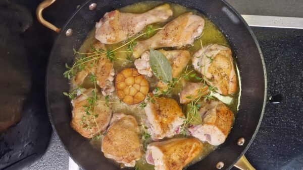 Chicken cooking with garlic, herbs, and liquid in a skillet